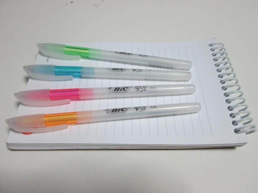 Four Bic Pens on Lined Notepad on White Background 