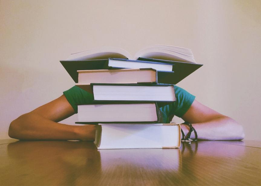 Person Hiding behind a Pile of Books at a Table 