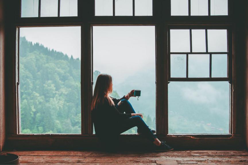 Woman seated at the window with coffee cup in hand looking at the view. 