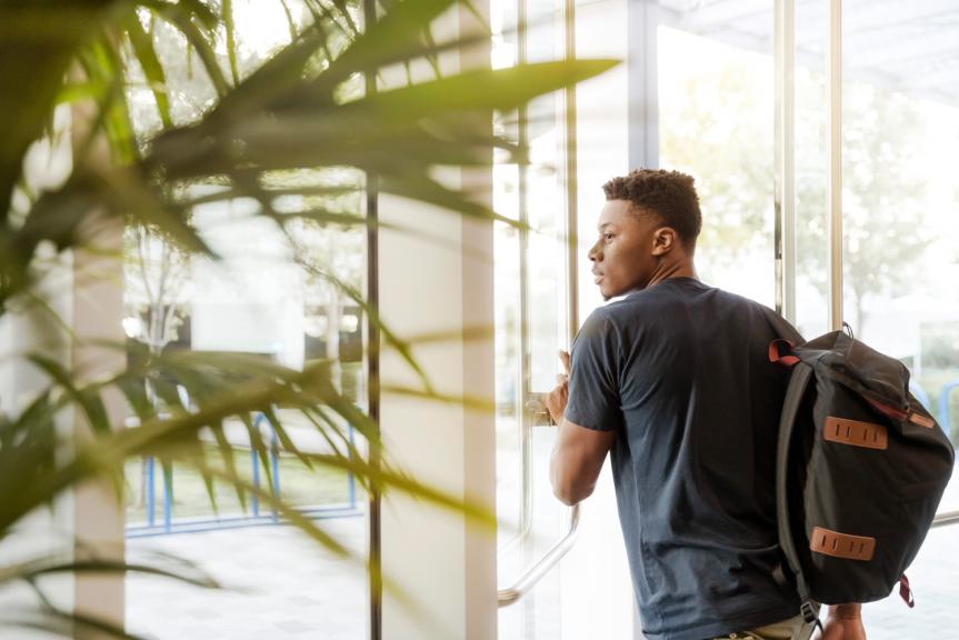 Student Wearing Backpack in building Walking next to Green Plant 